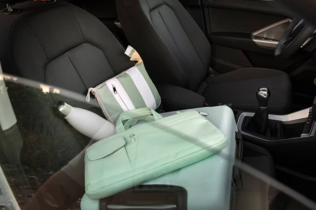 Interior of a car featuring two black seats, a striped bag, a mint green laptop case, and a stainless steel water bottle.