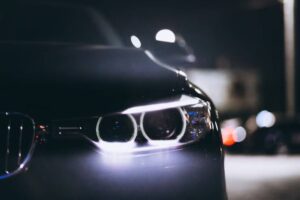Close-up of a sleek car's front headlights at night, glowing brightly against a dark background, highlighting its modern design.
