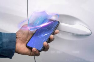 A hand holding a smartphone with a digital lock icon, poised near a car door handle, illustrating mobile vehicle access technology.