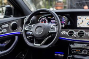 Interior view of a luxury car with a sleek steering wheel, digital dashboard, and navigation display, illuminated with blue accents.