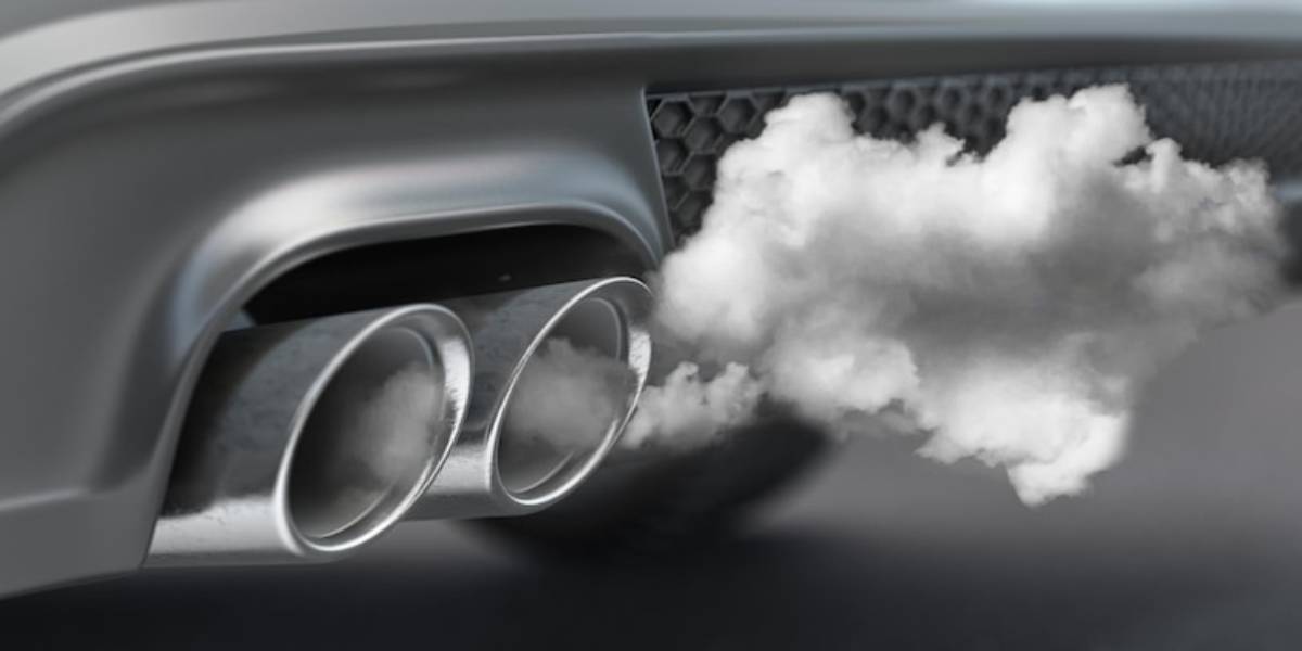 Close-up of a car's dual exhaust pipes emitting gray exhaust fumes, highlighting emissions from a vehicle.