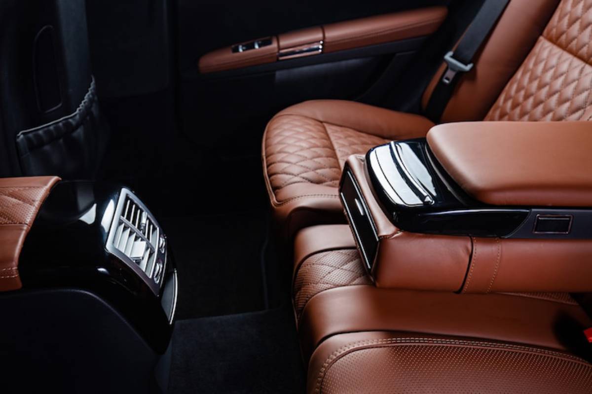 Luxurious car interior featuring quilted brown leather seats and a sleek, glossy black armrest with air vents.