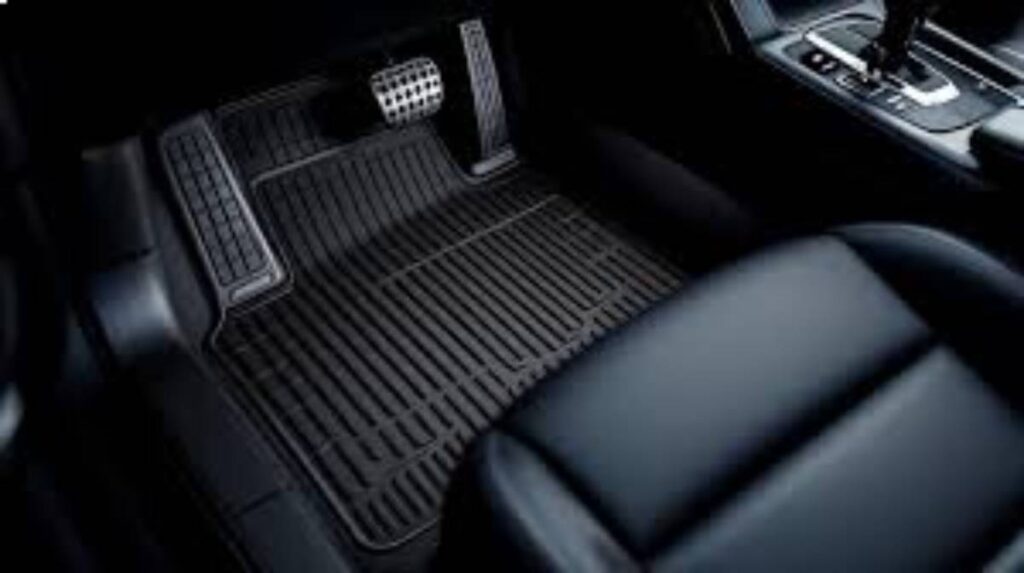 Close-up of a black rubber car floor mat with textured design, showing a foot pedal and part of the vehicle's interior.