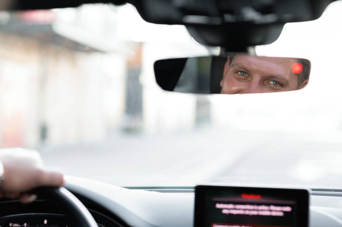 A driving scene featuring a hand on the steering wheel, a view through the windshield, and a dashboard display.