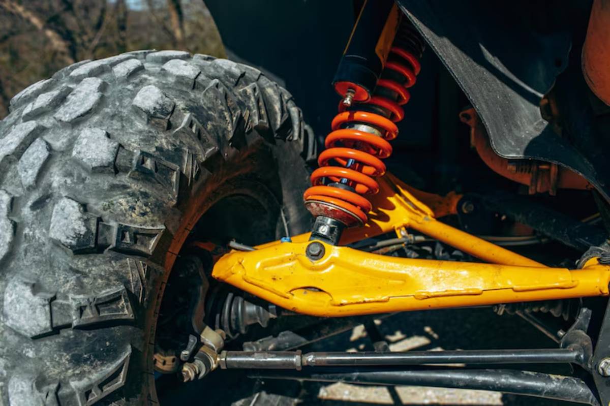 Close-up of a rugged off-road vehicle's suspension system, featuring an orange coil spring, yellow arm, and large tire tread.