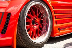 Close-up of a glossy red car wheel with a multi-spoke design, showcasing sleek tire and vibrant body color.
