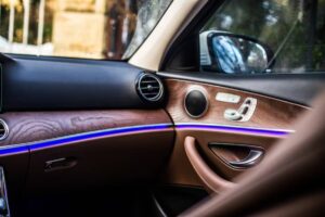 A sleek car dashboard featuring a wood finish and ambient blue lighting, with air vents showcasing modern design elements.