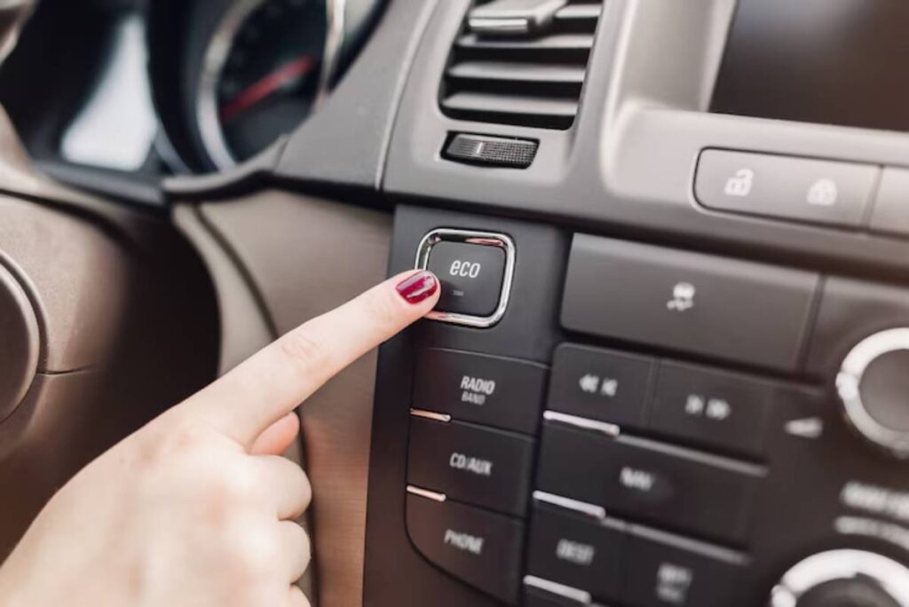 A hand with red nail polish pressing the "eco" button on a car's dashboard for fuel efficiency.