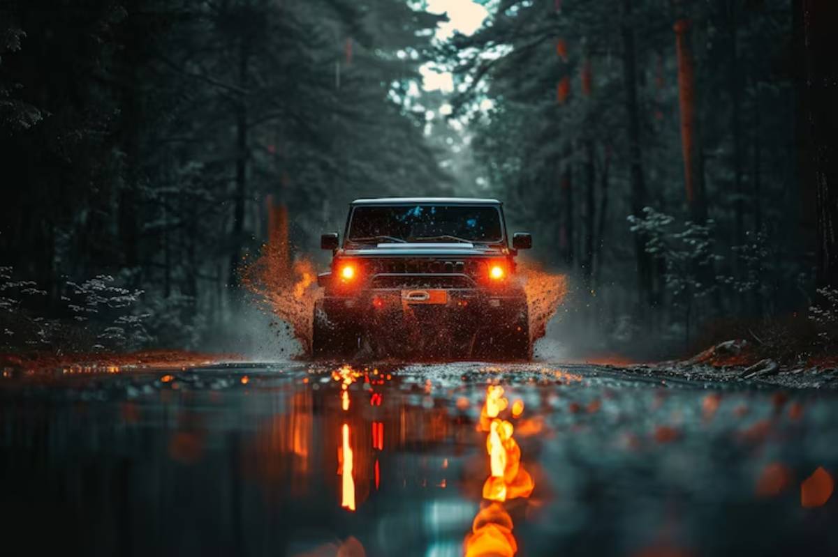 A rugged SUV splashes through a dark, forested road, illuminated by its orange headlights reflecting off wet pavement.