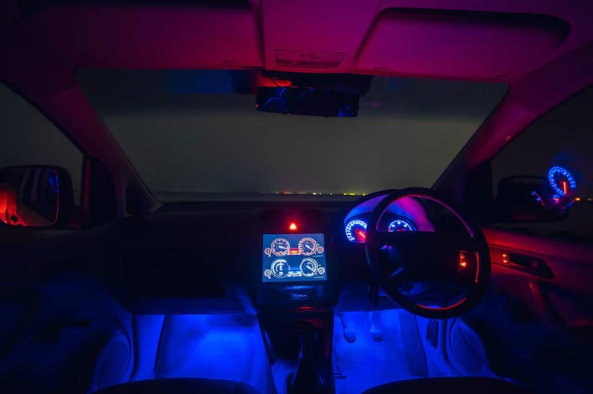 Interior view of a car with vibrant blue and red ambient lighting, featuring a digital display and illuminated gauges against a dark background.