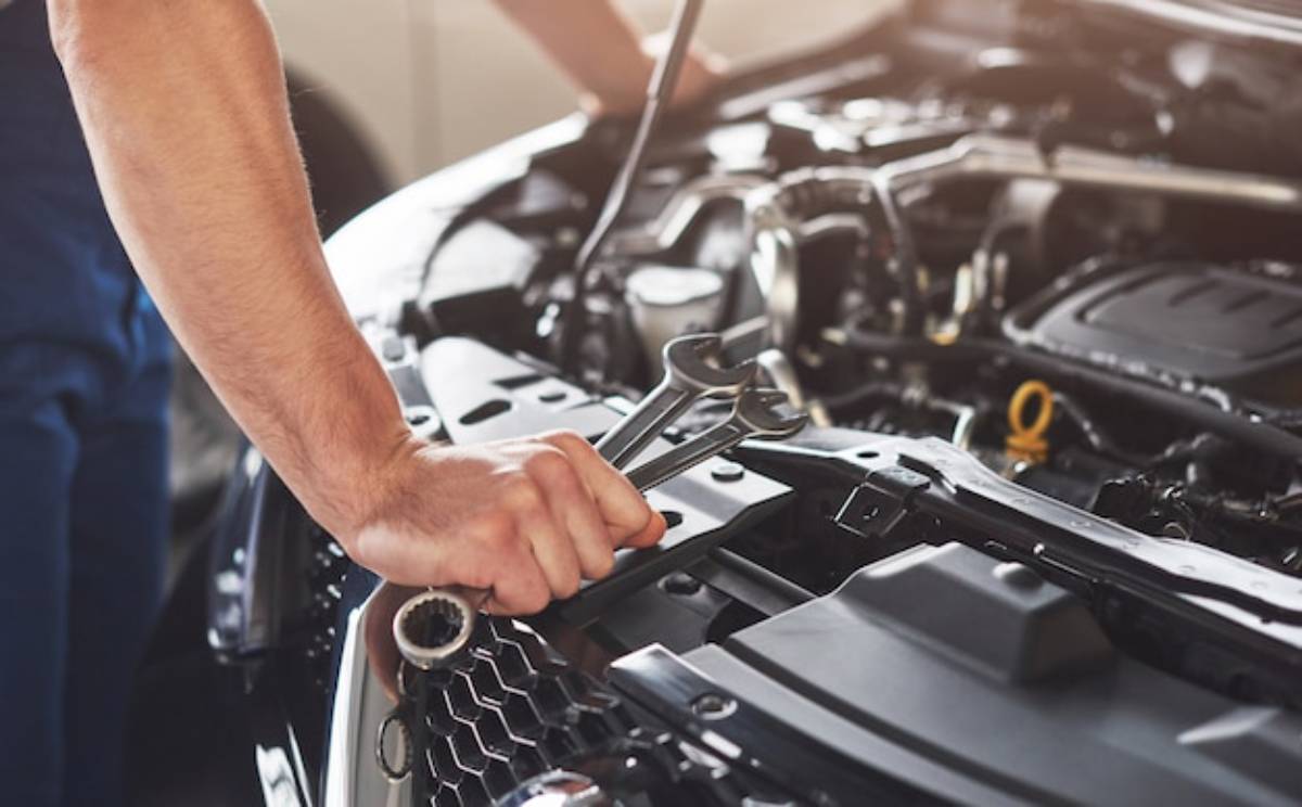 A mechanic's hand holding a wrench, working under the hood of a car with an open engine compartment, focused on repairs.