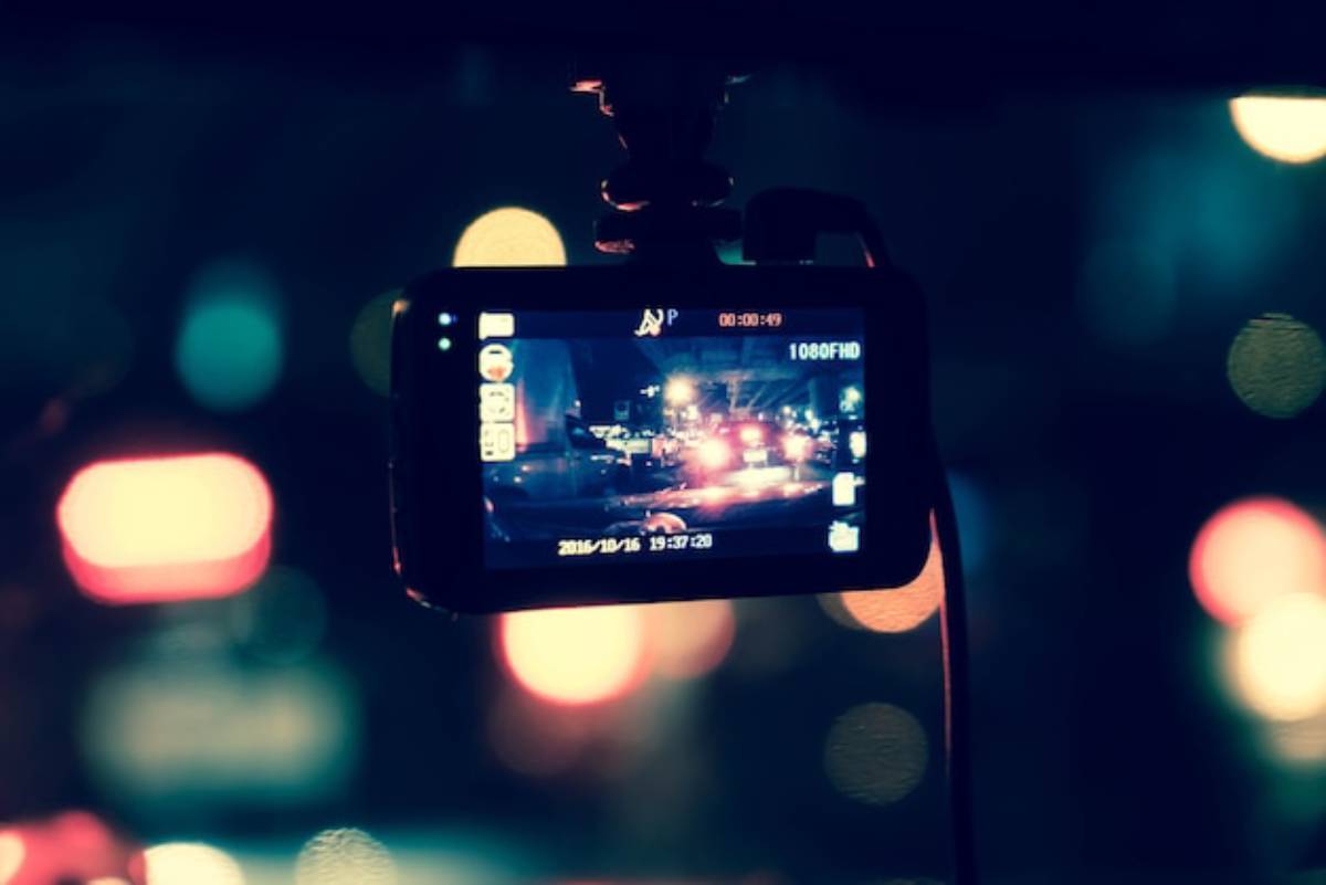 A dashboard camera displaying a nighttime view of city traffic with colorful bokeh lights in the background.