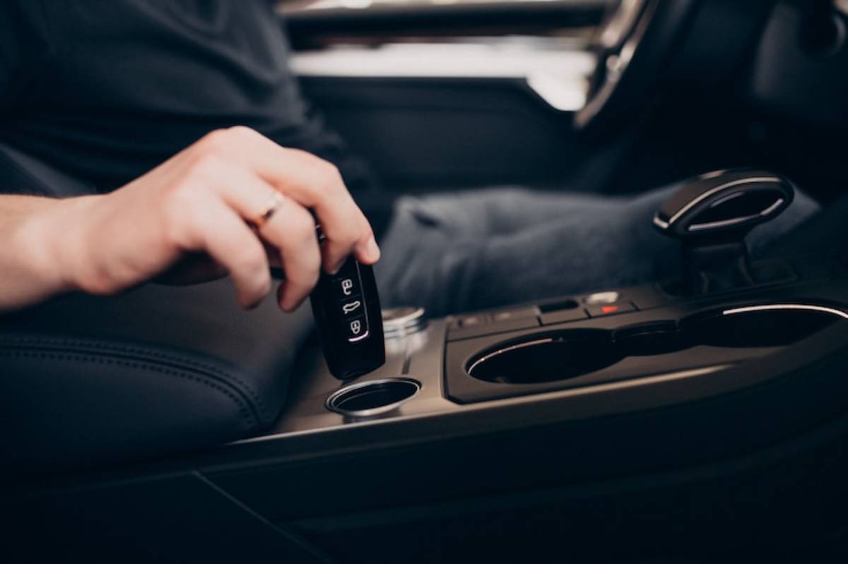 A close-up of a hand holding a car key fob, reaching into the console of a modern vehicle.