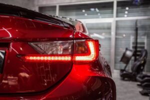 Close-up of a shiny red car's rear tail light in a modern garage, showcasing sleek design and illuminated LED features.