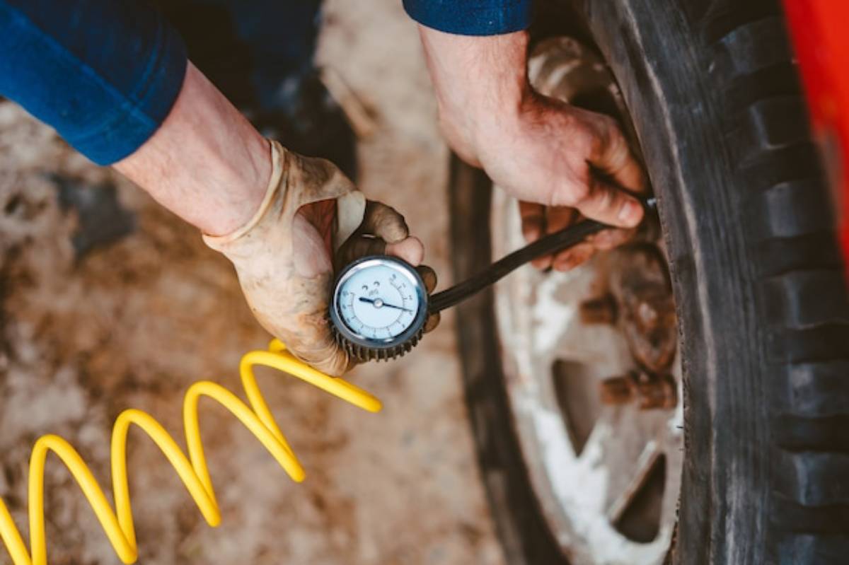 A person inflating a car tire using a hose, focusing on the valve and their hand, with the car partially visible in the background.