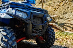 Close-up of a blue all-terrain vehicle (ATV) front, showcasing its rugged tire and protective features against a natural background.