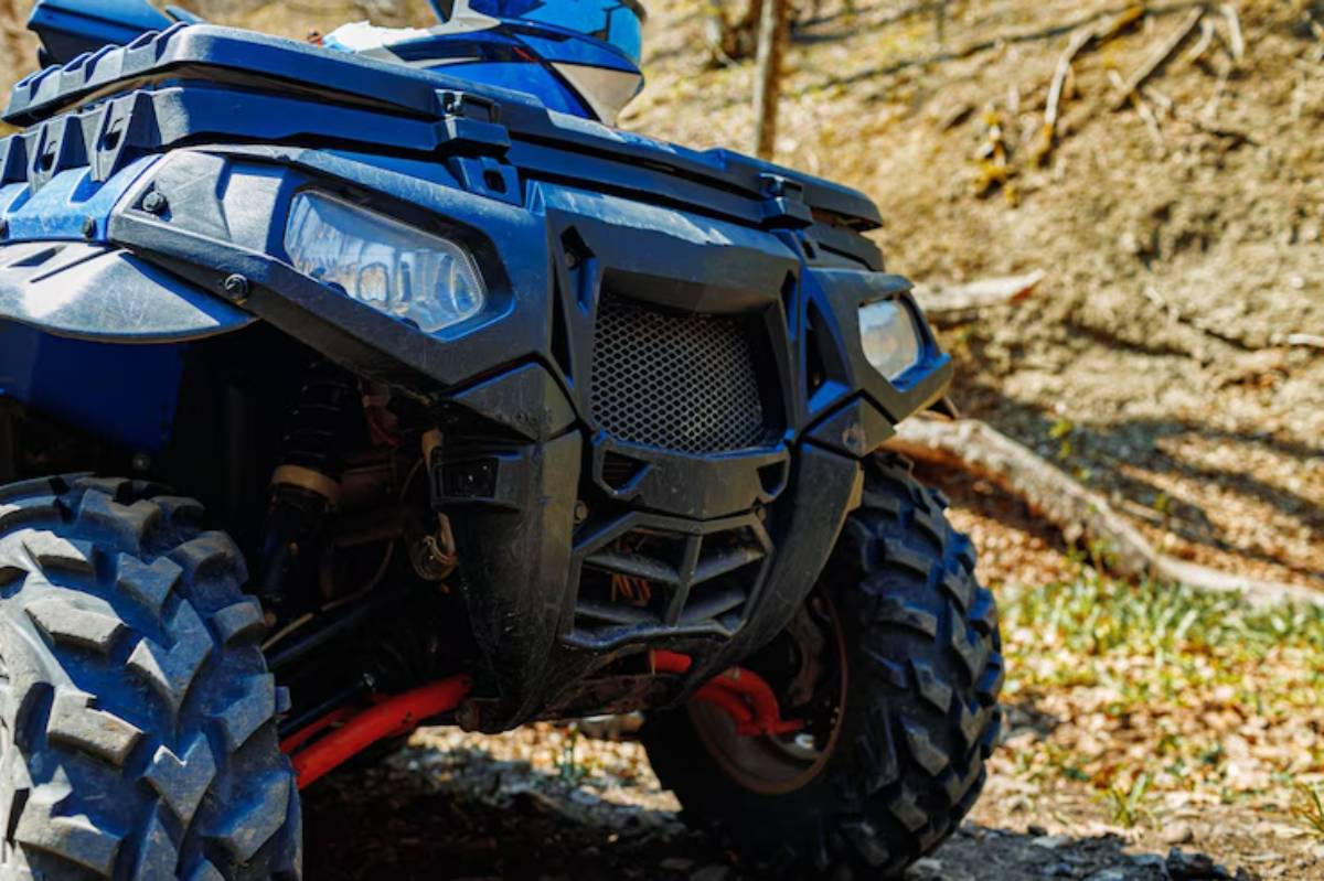 Close-up of a blue all-terrain vehicle (ATV) front, showcasing its rugged tire and protective features against a natural background.