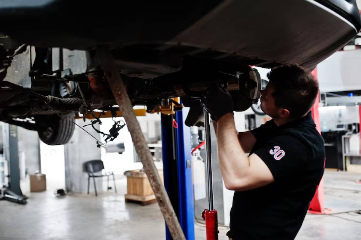 A car repair shop with a white car on a lift, mechanics working, and tools cluttered on a nearby red workbench.