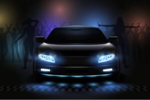 A sleek black car with glowing headlights is illuminated against a dark backdrop, surrounded by silhouettes of dancing figures.