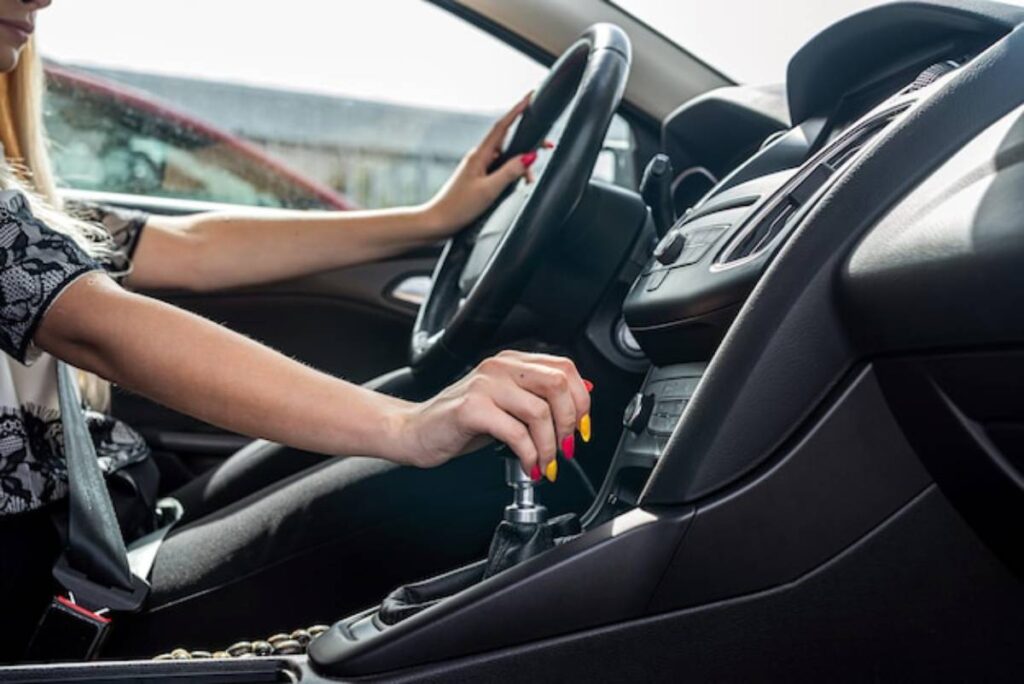 A woman with stylish nail polish shifts gears in a car, focused on driving, with a modern dashboard visible.