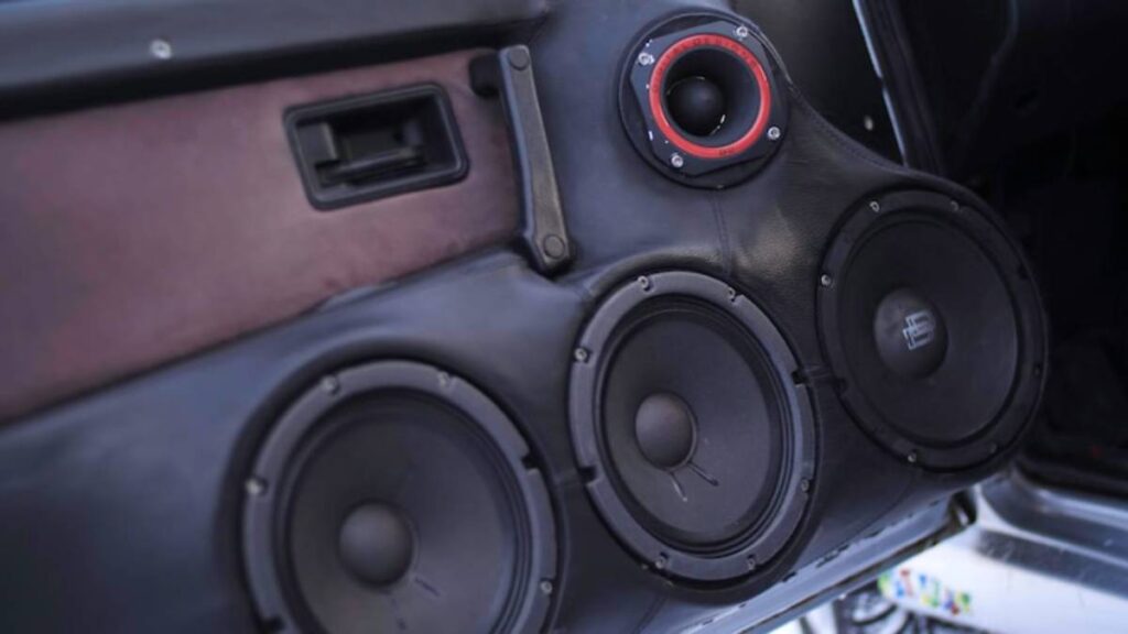 Close-up of a black car audio speaker system, featuring three large speakers and a small tweeter, integrated into a vehicle's interior.