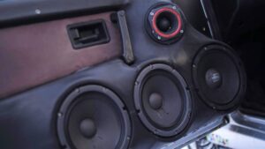 Close-up of a black car audio speaker system, featuring three large speakers and a small tweeter, integrated into a vehicle's interior.