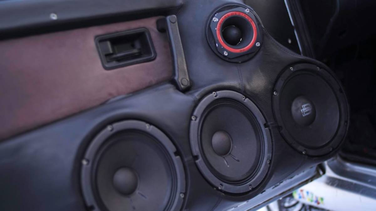 Close-up of a black car audio speaker system, featuring three large speakers and a small tweeter, integrated into a vehicle's interior.