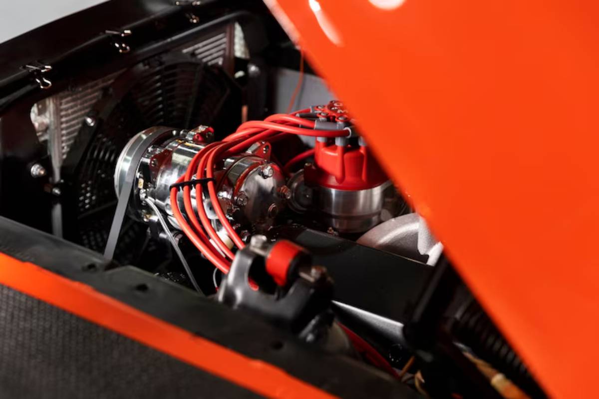 Close-up of a vibrant orange car engine, showcasing polished components, red wires, and a cooling fan behind the open hood.