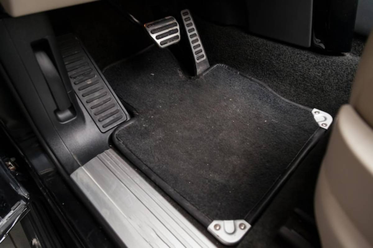 Close-up of a car's footwell featuring a black floor mat, metal pedal covers, and accelerator, brake, and clutch pedals.