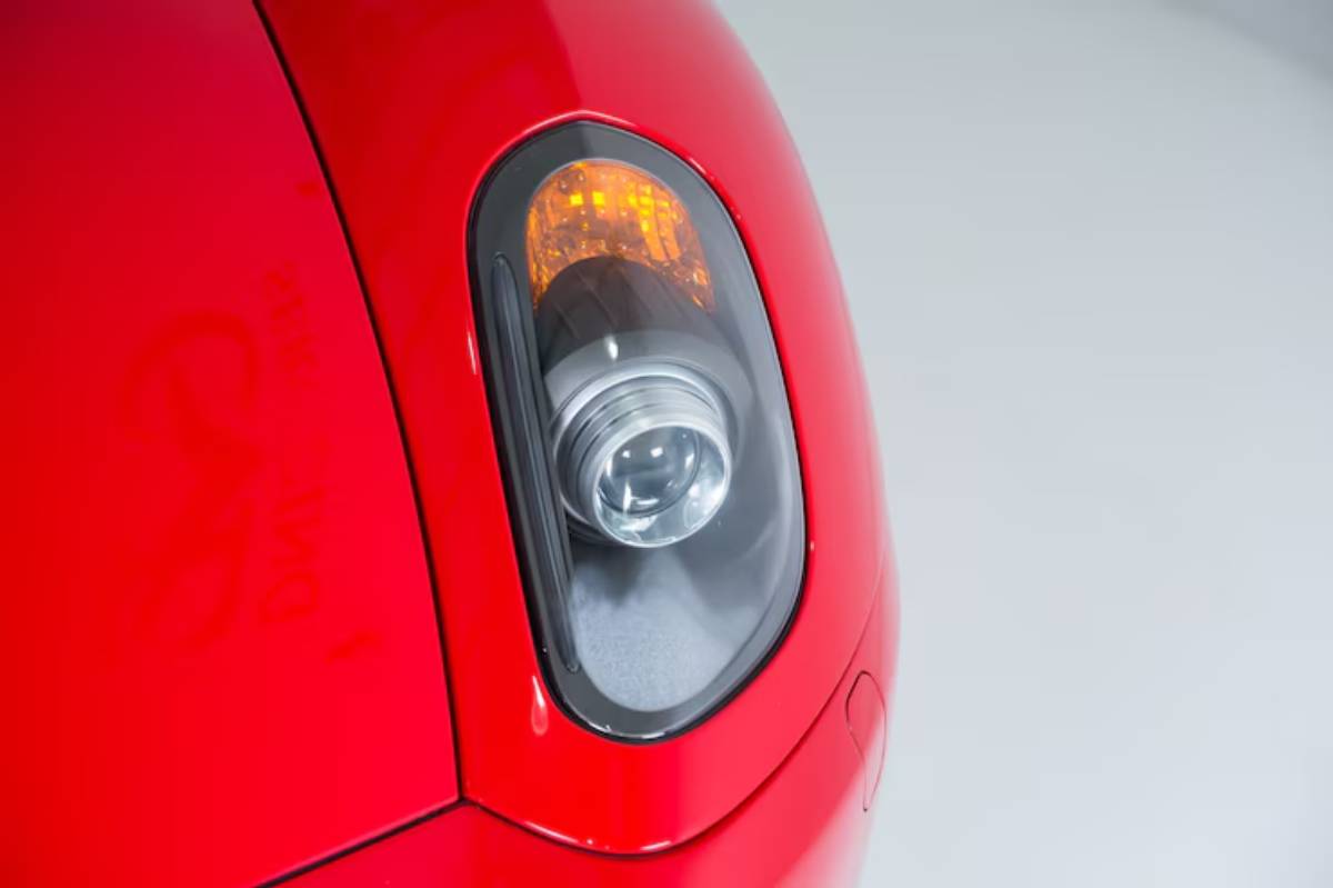 Close-up of a red car's headlight featuring a rounded design and amber indicator, set against a neutral background.