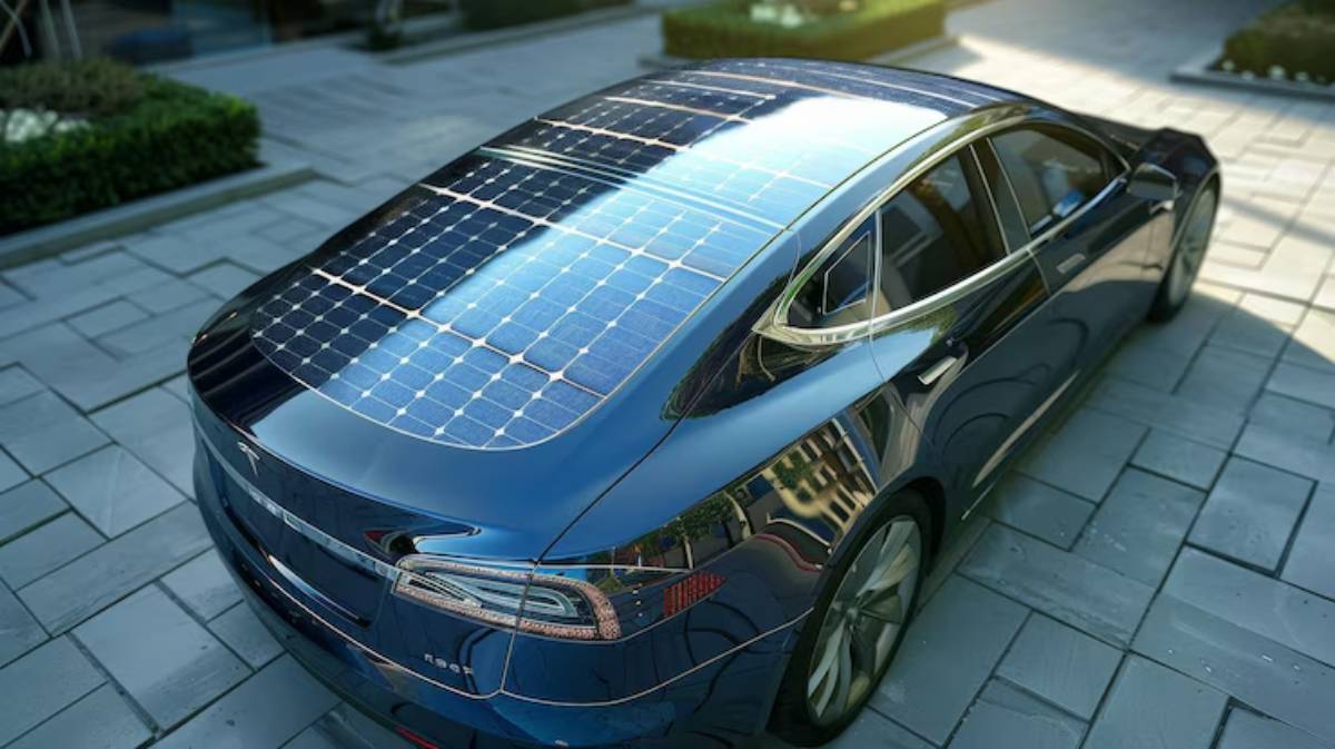 A sleek blue electric car with a solar panel-covered roof parked on a stone-paved surface, surrounded by greenery.
