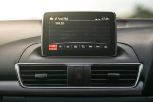 A driver's hand reaches toward a modern car dashboard touchscreen, highlighting its sleek design and empty display.